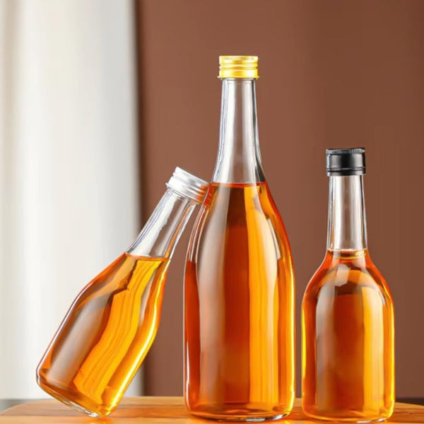 Clear glass bottles with screw caps filled with amber liqueur and oil on a wooden board