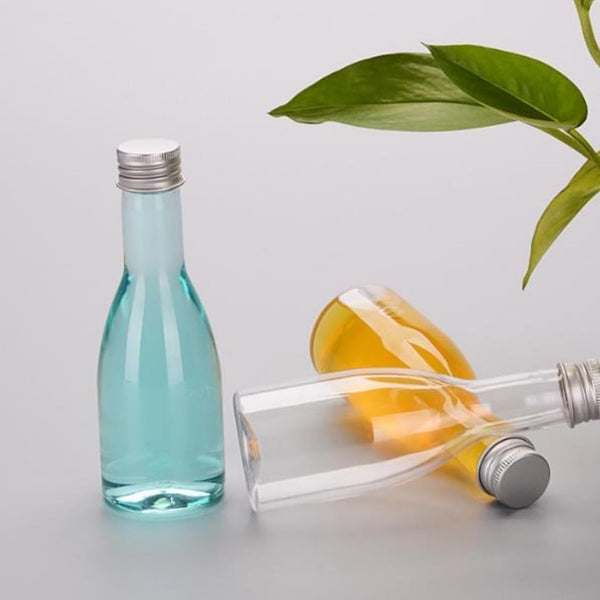 200 ml glass bottles with silver screw caps holding blue and amber liquids beside a green plant
